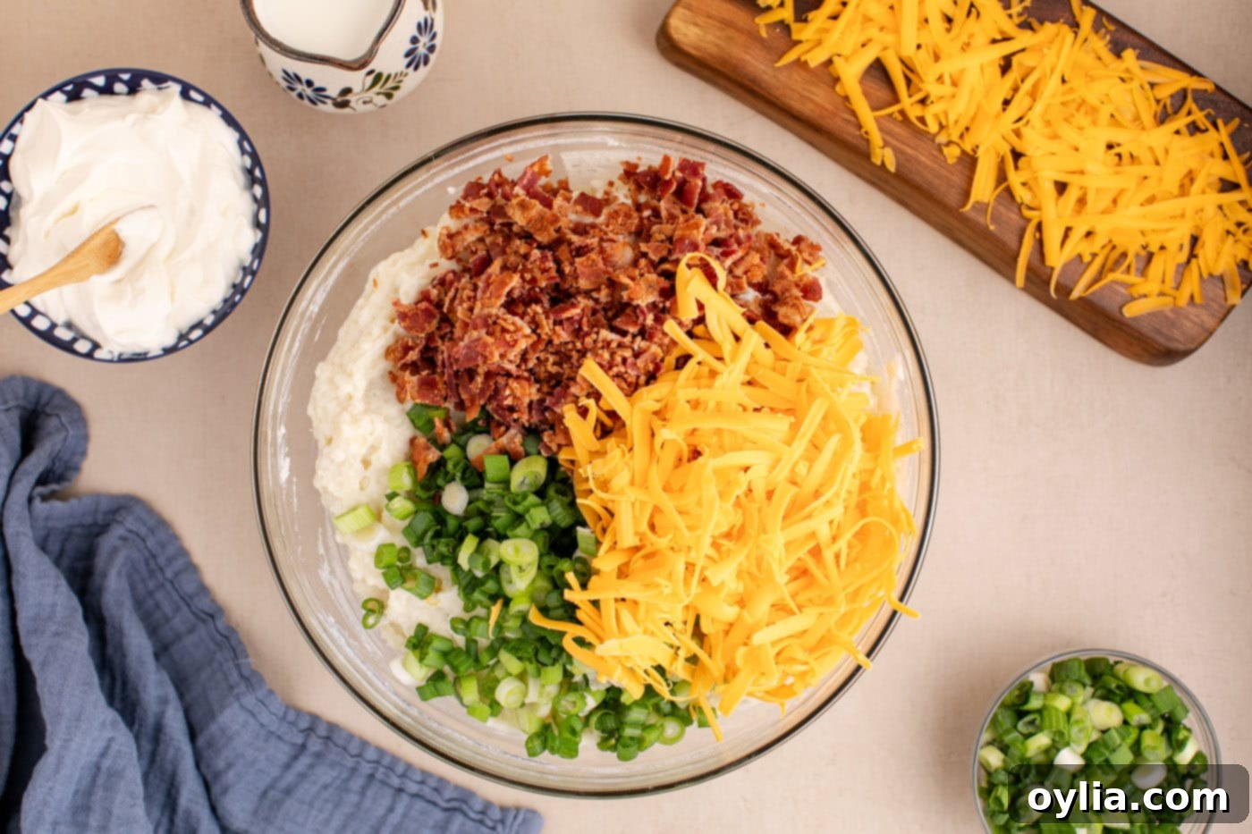 Crumbled bacon, shredded cheddar cheese, and sliced green onion added to the creamy twice baked potato filling in a bowl.