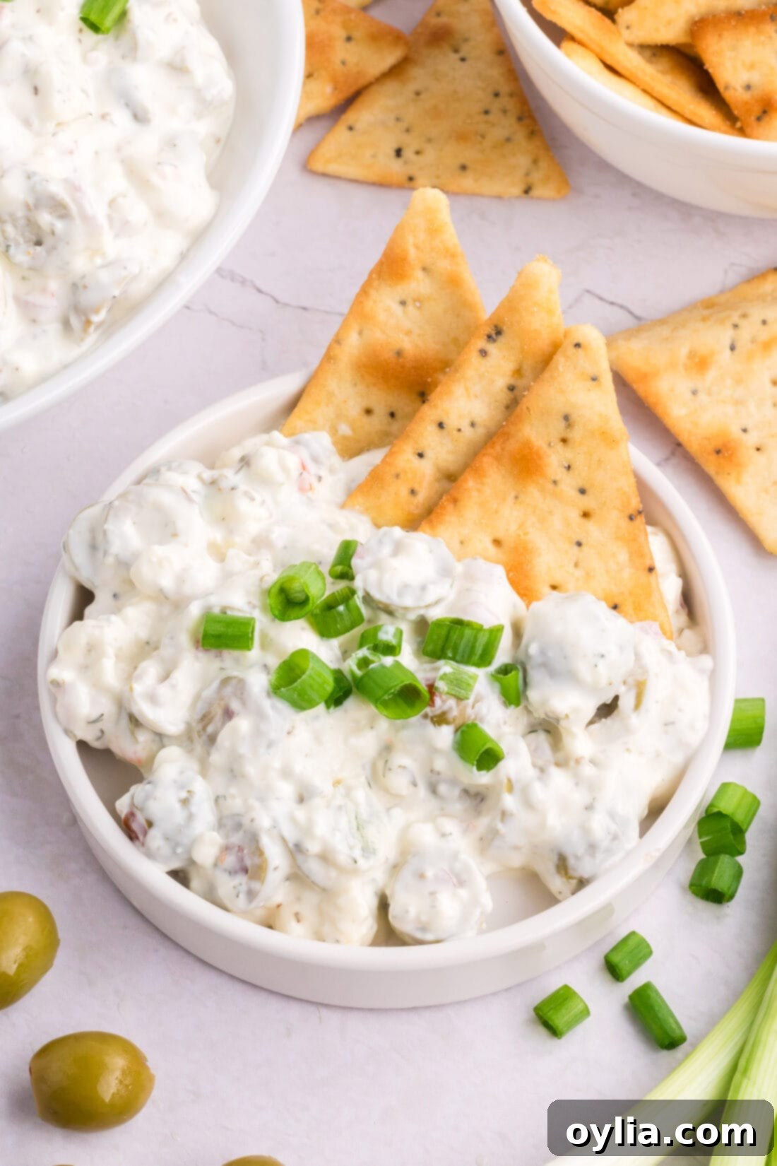 Signature Dirty Martini Dip 3 Dirty Martini Dip on a plate with an assortment of crackers and a few whole olives