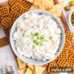 Signature Dirty Martini Dip 10 Bowl of Dirty Martini Dip on a board with pretzels and crackers around it, garnished with olives and green onions.