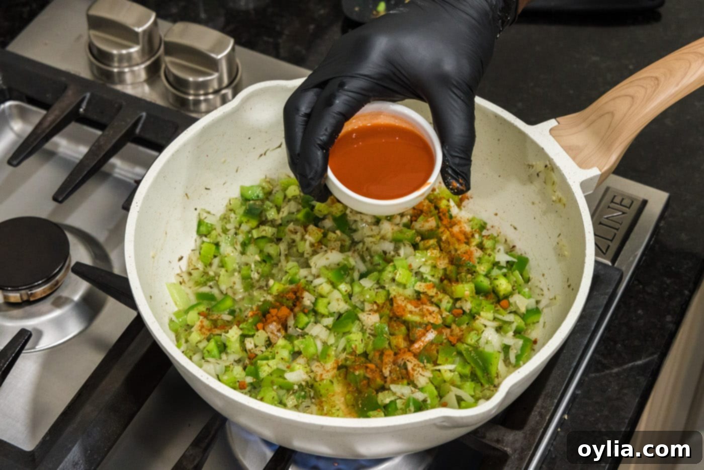 pouring hot sauce and spices into skillet of green pepper, onion, and celery