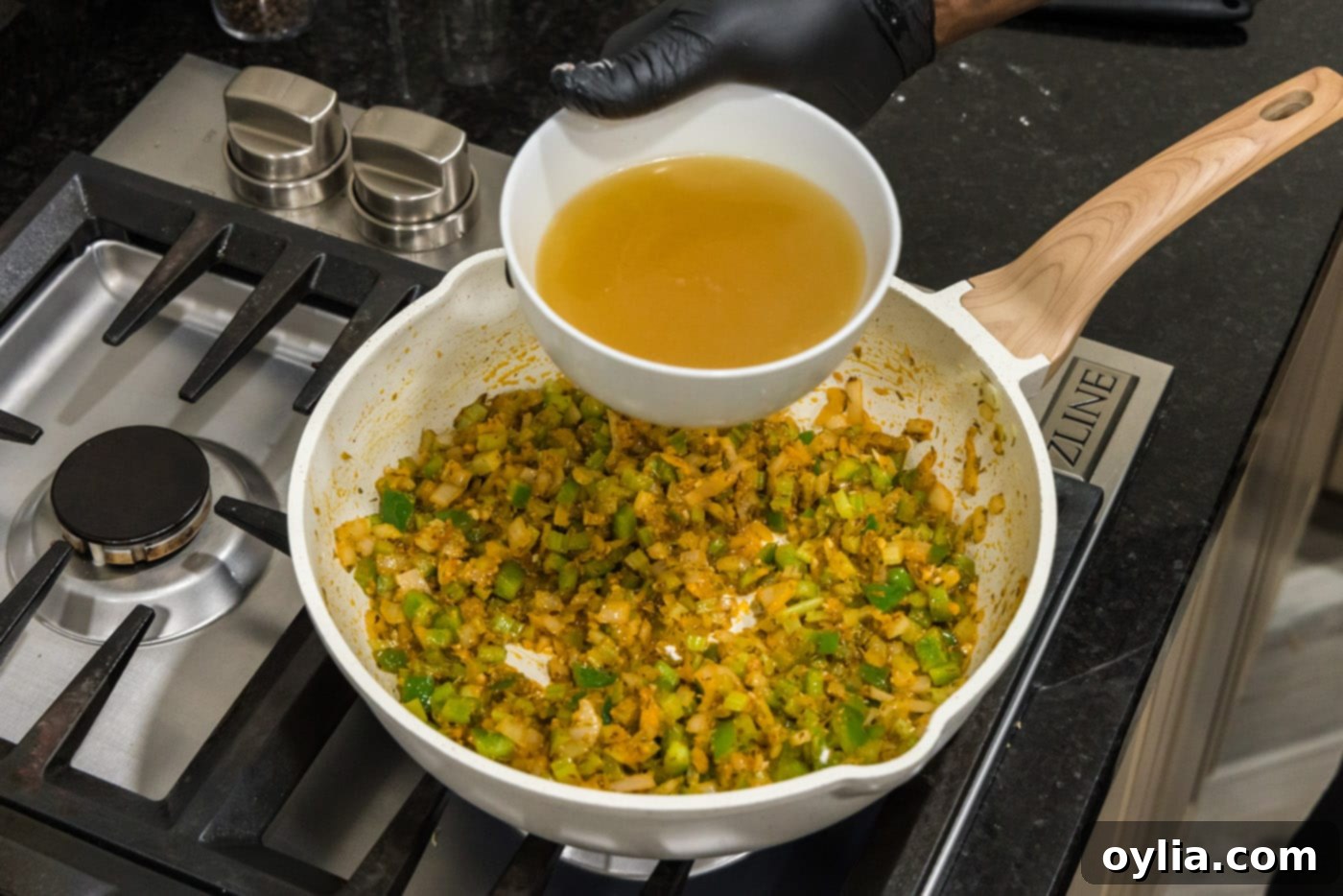 pouring chicken stock into skillet of shrimp creole