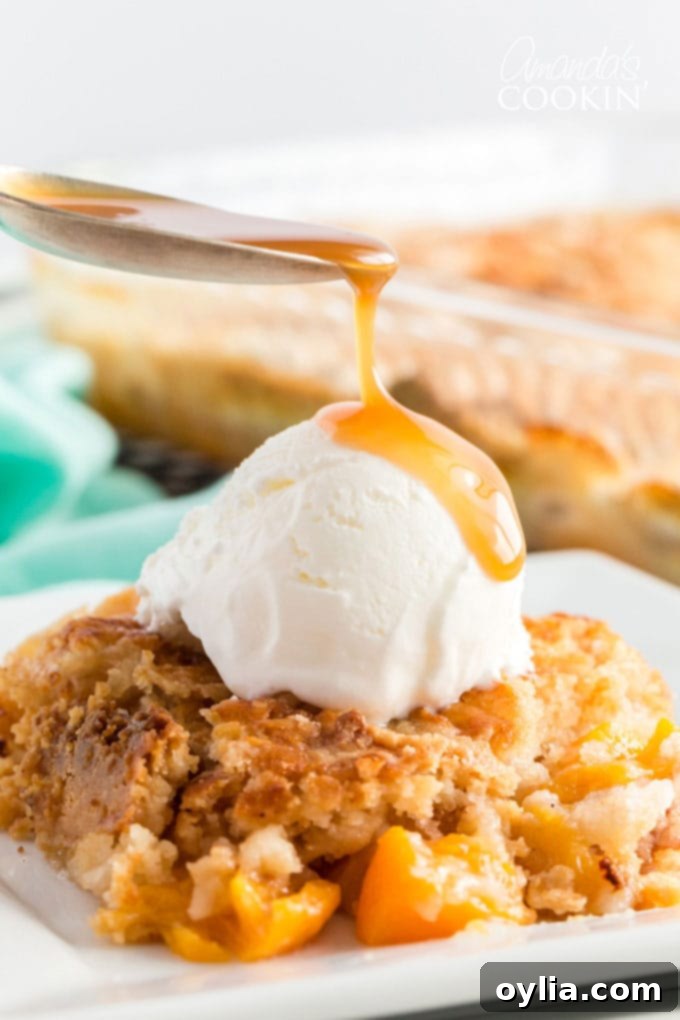 Spoon dripping caramel onto vanilla ice cream on a warm slice of peach cobbler dump cake, ready to be served.