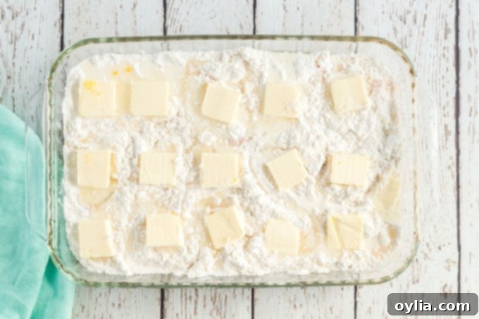 Uncooked peach dump cake in a baking pan, with butter pats strategically placed over the dry cake mix layer, preparing for baking.