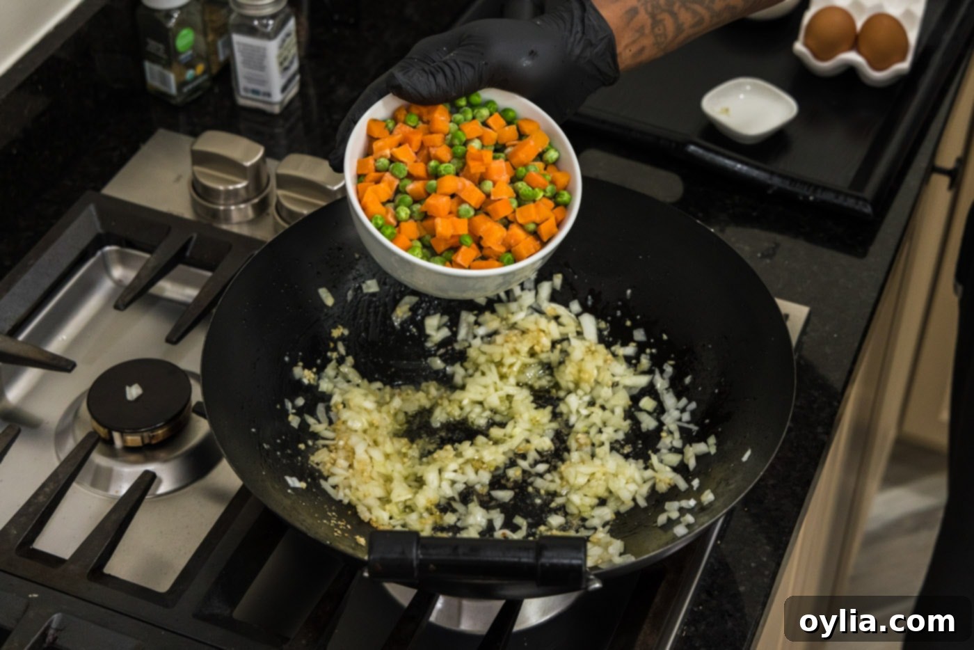 adding frozen peas and carrots to a wok with onion and garlic