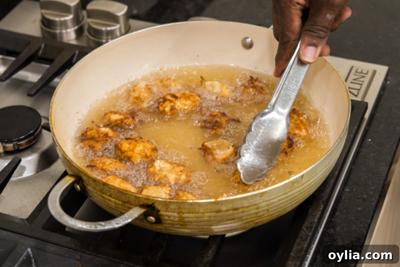 Tongs flipping fried pork pieces in hot oil for even cooking