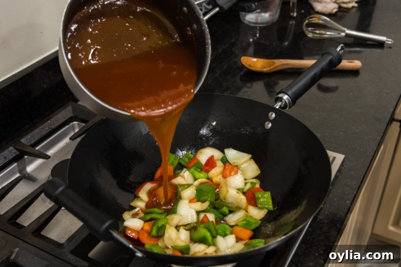 Sweet and sour sauce being poured over stir-fried vegetables in a wok