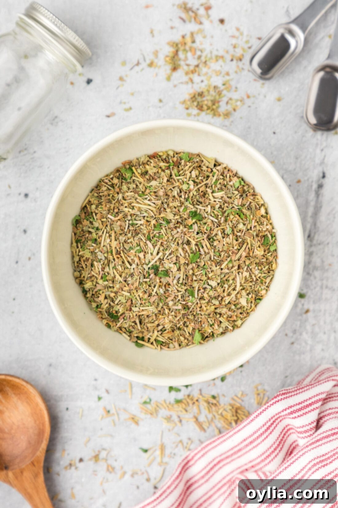 Classic Italian Herb Blend 7 A rustic bowl of homemade Italian seasoning, accompanied by a set of measuring spoons and a ready-to-use spice jar.