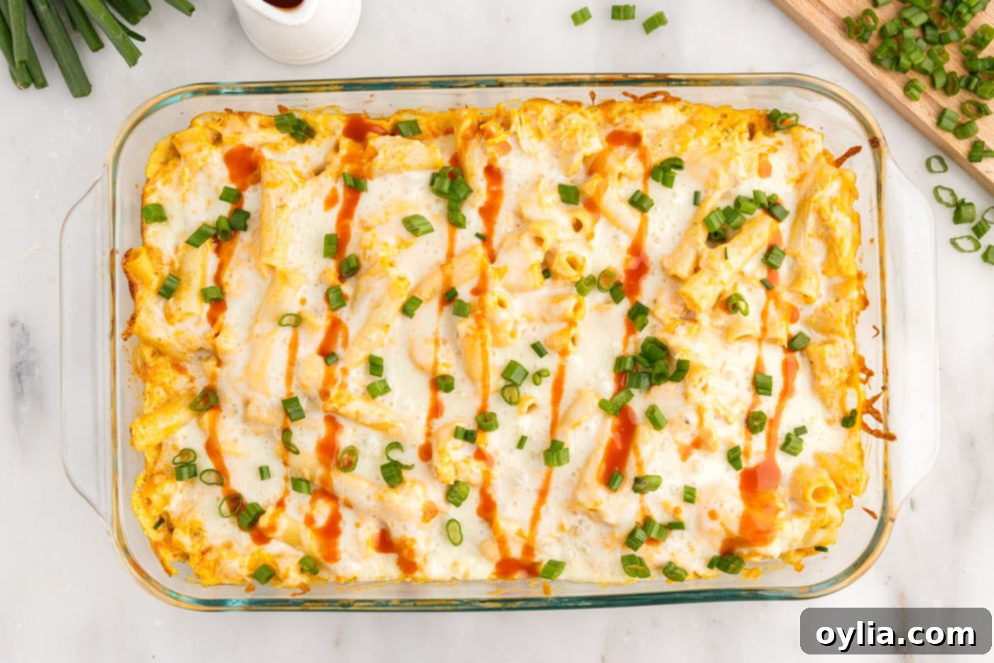 Overhead view of buffalo chicken casserole garnished with extra hot sauce and sliced green onions, ready to serve.