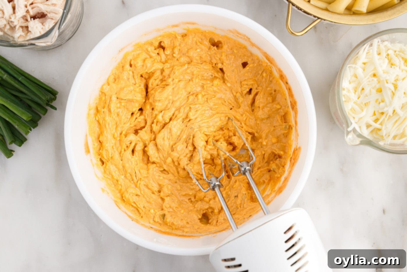Mixing the buffalo chicken casserole sauce ingredients with a hand mixer until smooth and creamy.