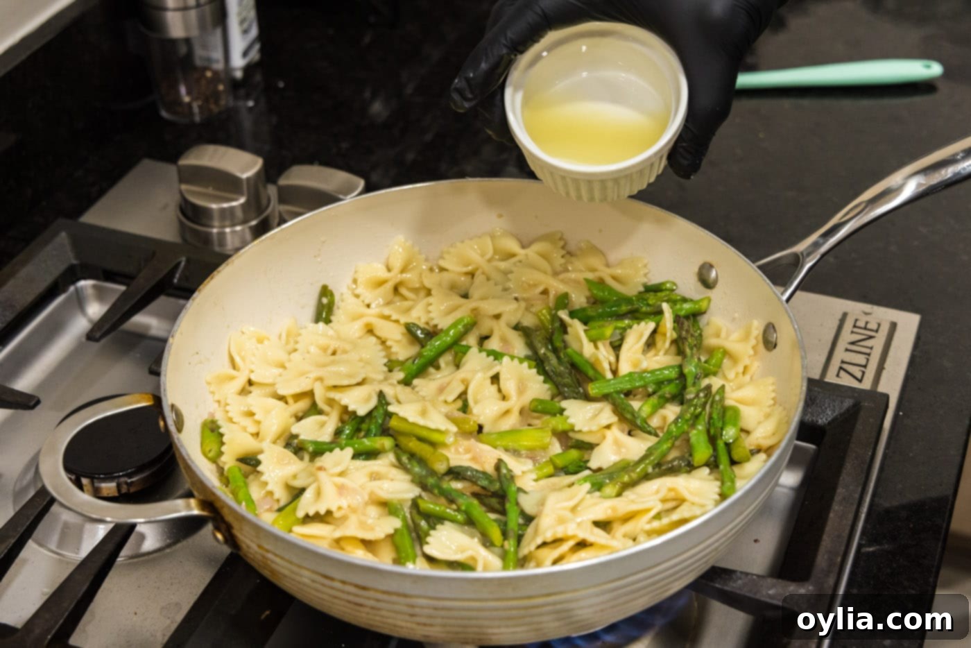 Fresh lemon juice being poured over the asparagus pasta in the skillet for a final bright flavor.