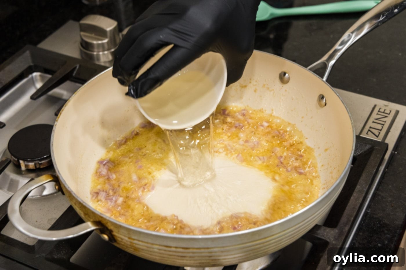 White wine being poured into a skillet with butter, garlic, and shallots, starting the deglazing process.