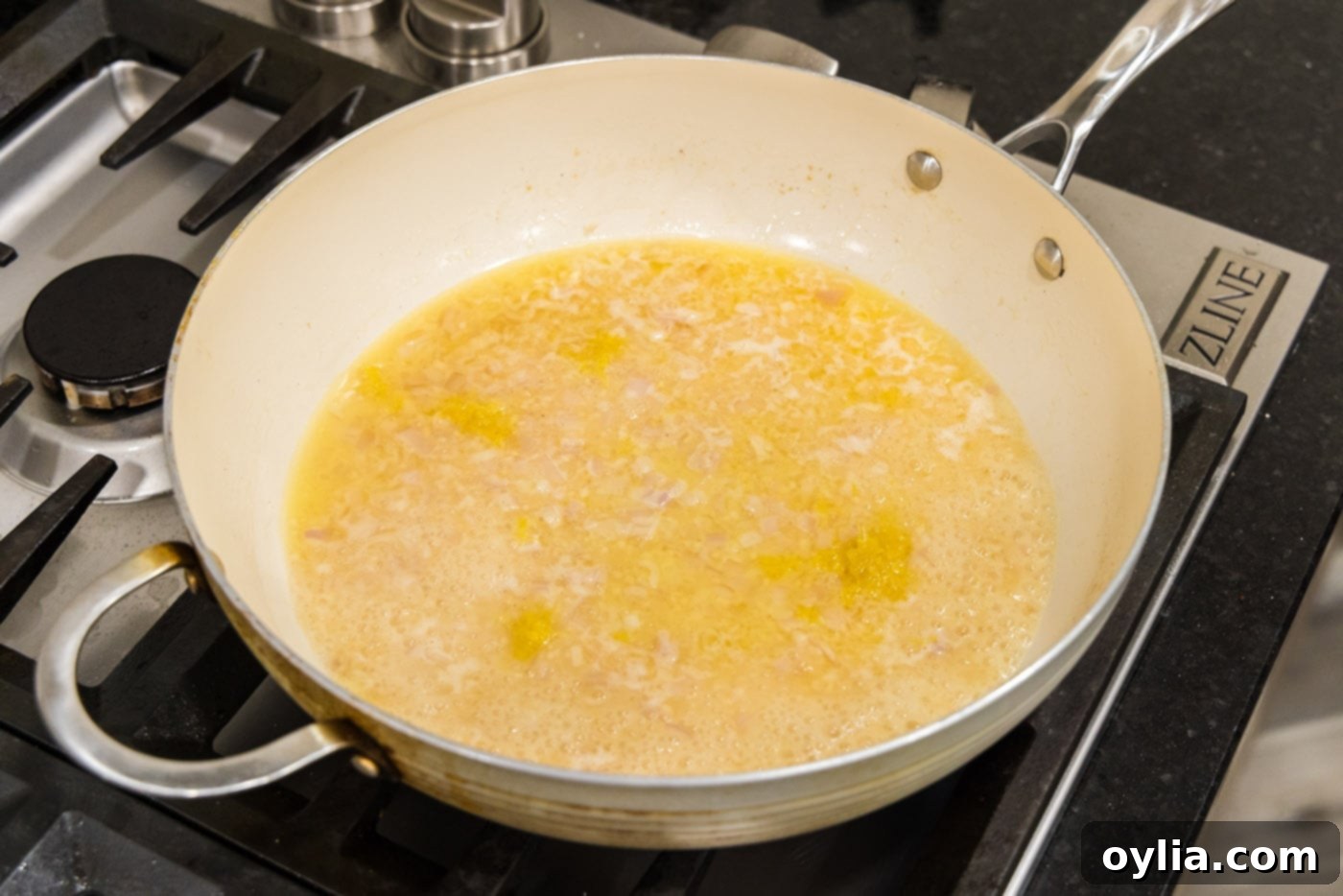The white wine sauce for pasta simmering in the skillet, infused with garlic, shallots, and lemon zest.