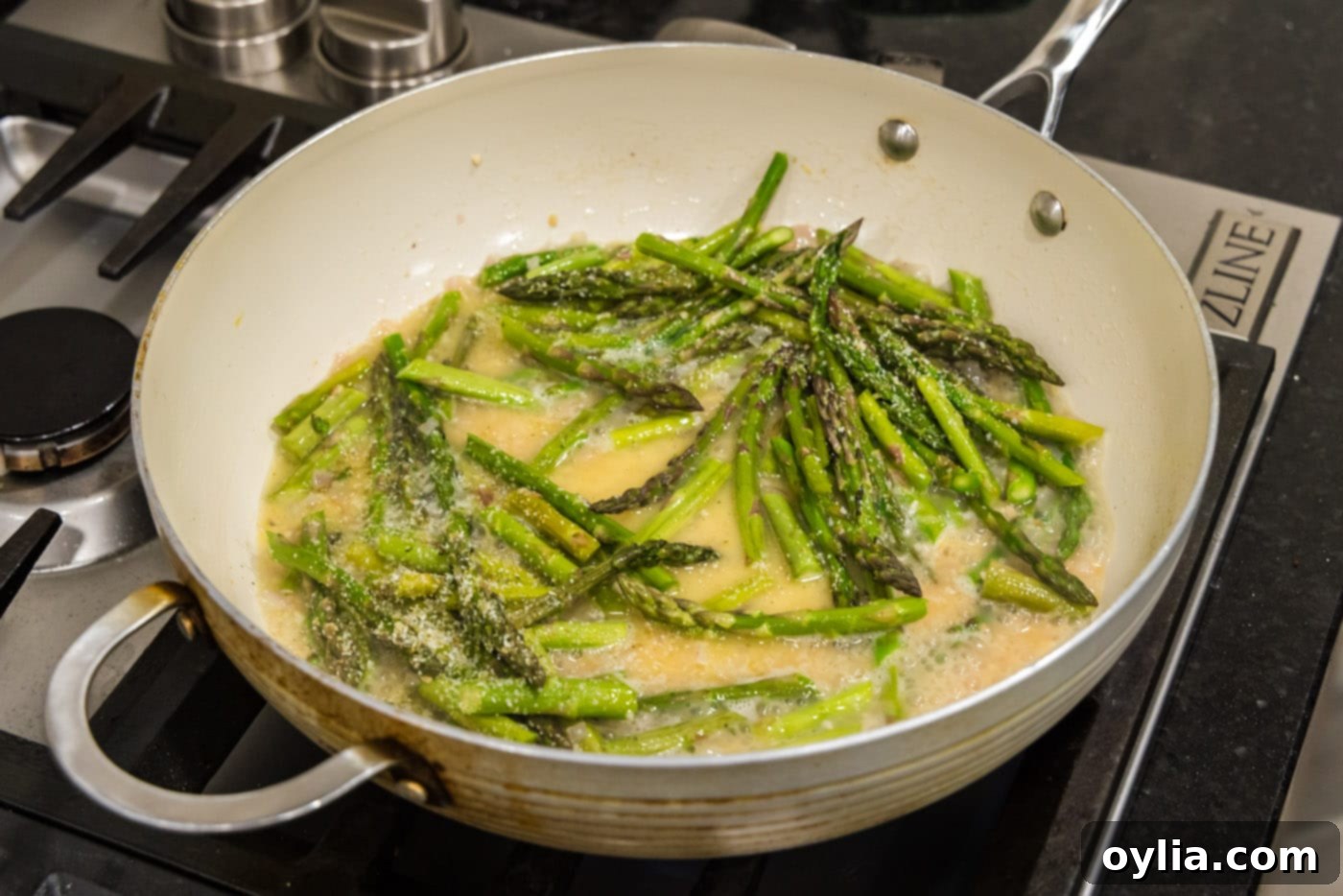 Fresh asparagus added to the simmering butter and white wine sauce mixture in the skillet.