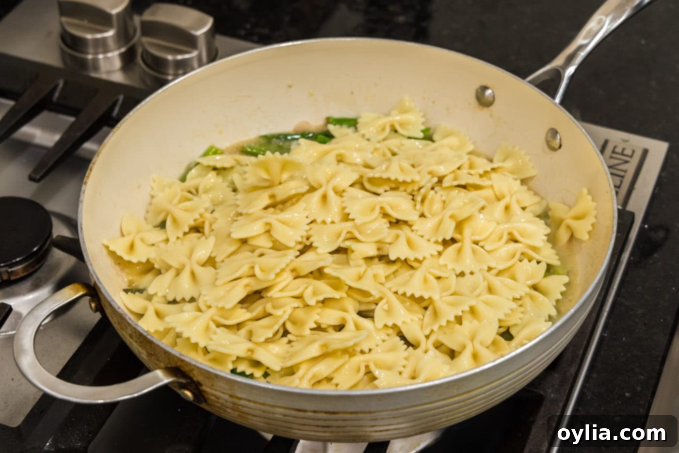Cooked bowtie pasta being added to the buttery asparagus sauce in the skillet and tossed.