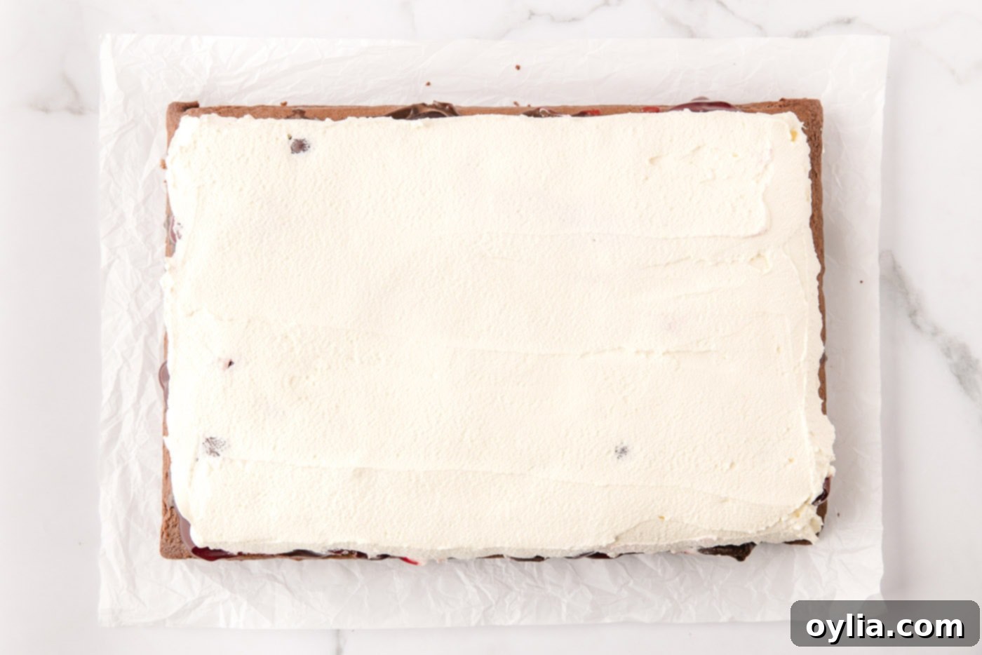 Smooth layer of whipped cream spread over the cherry pie filling on the Black Forest Poke Cake.