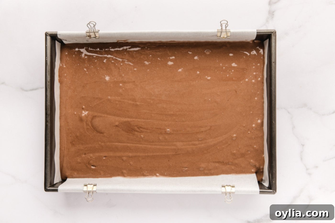 Chocolate cake mix being poured into a 13x9 inch baking pan, ready for the oven.
