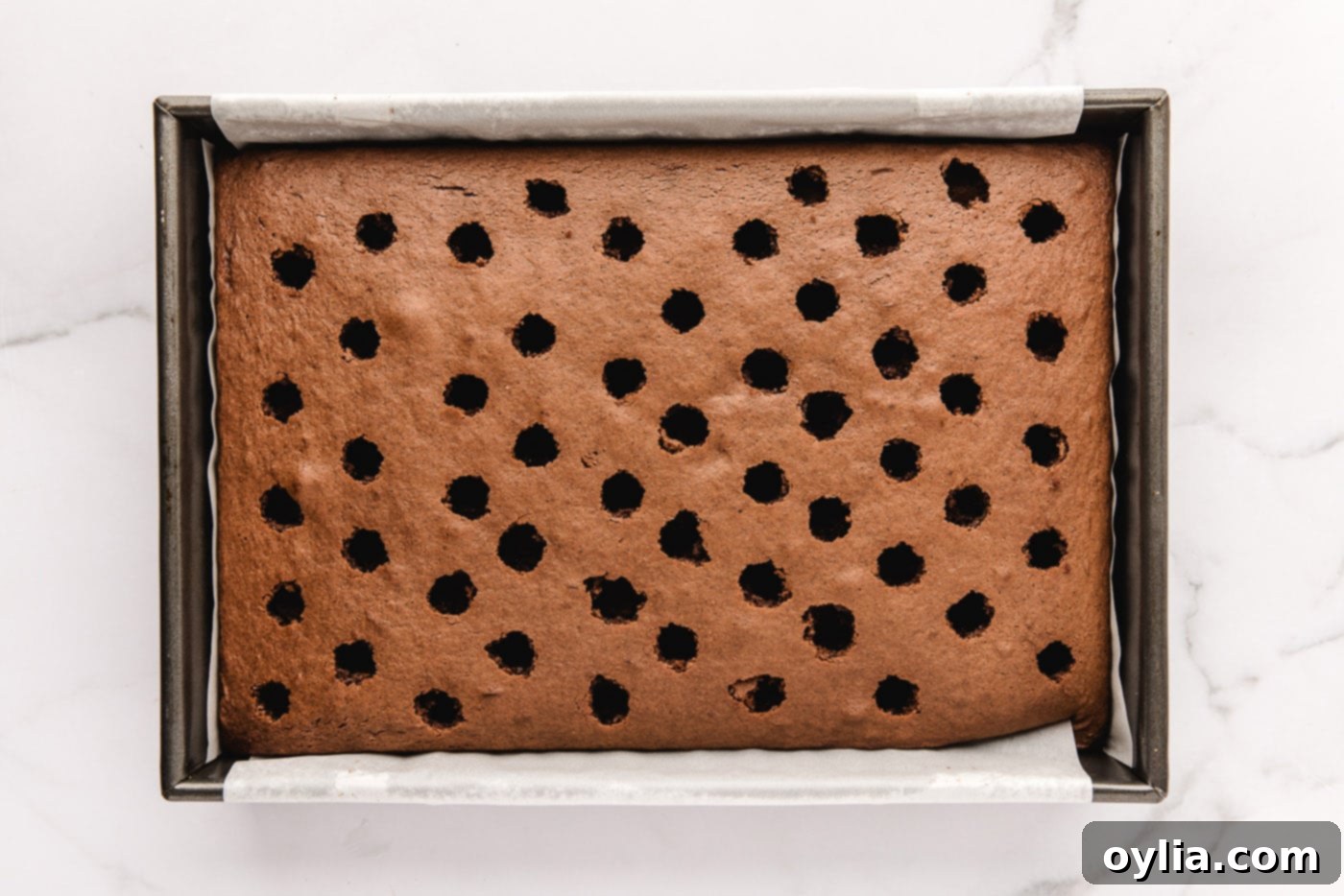 Close-up of a chocolate cake with holes poked evenly across its surface using the end of a wooden spoon.