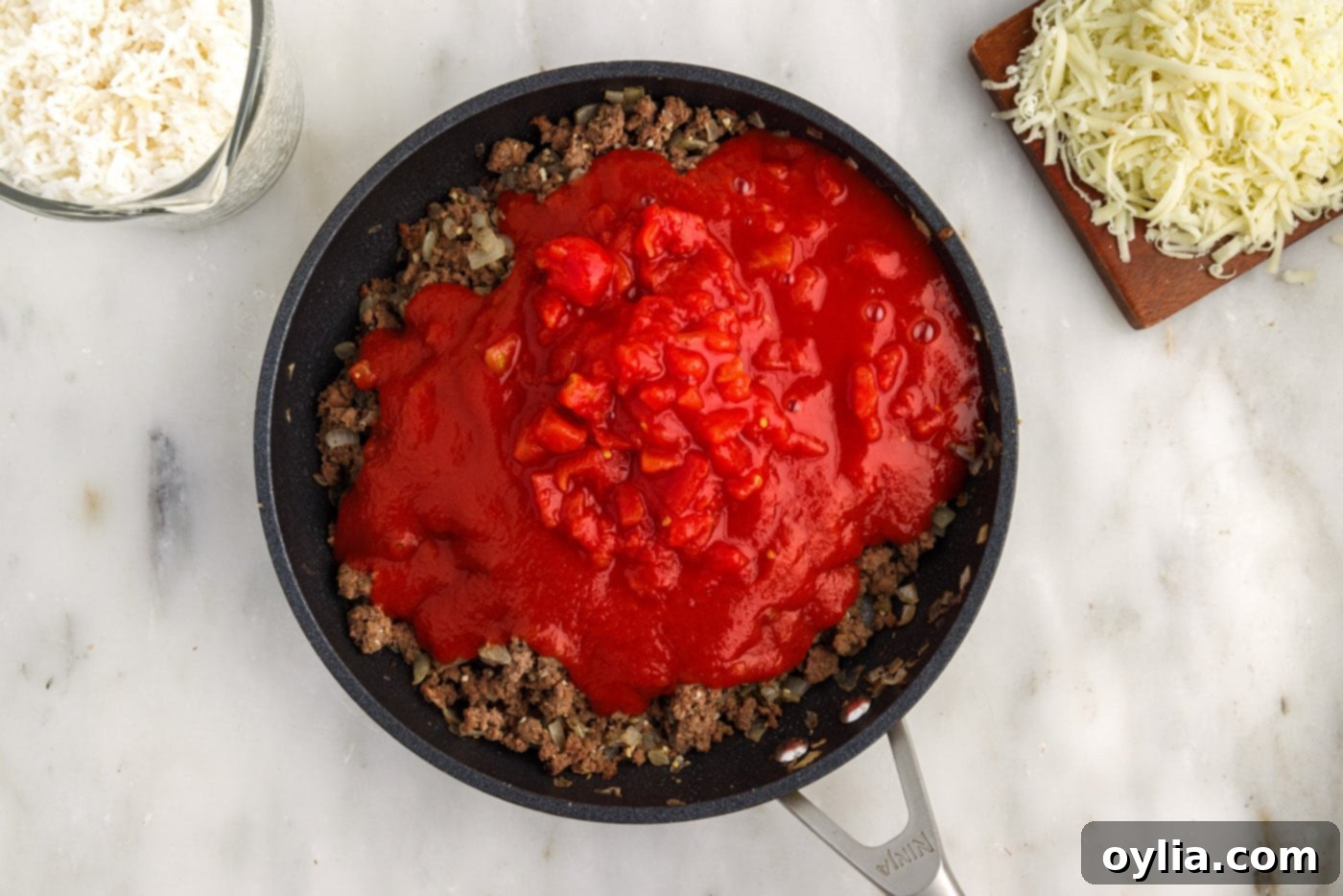 tomato sauce and diced tomatoes added on top of ground beef mixture in skillet