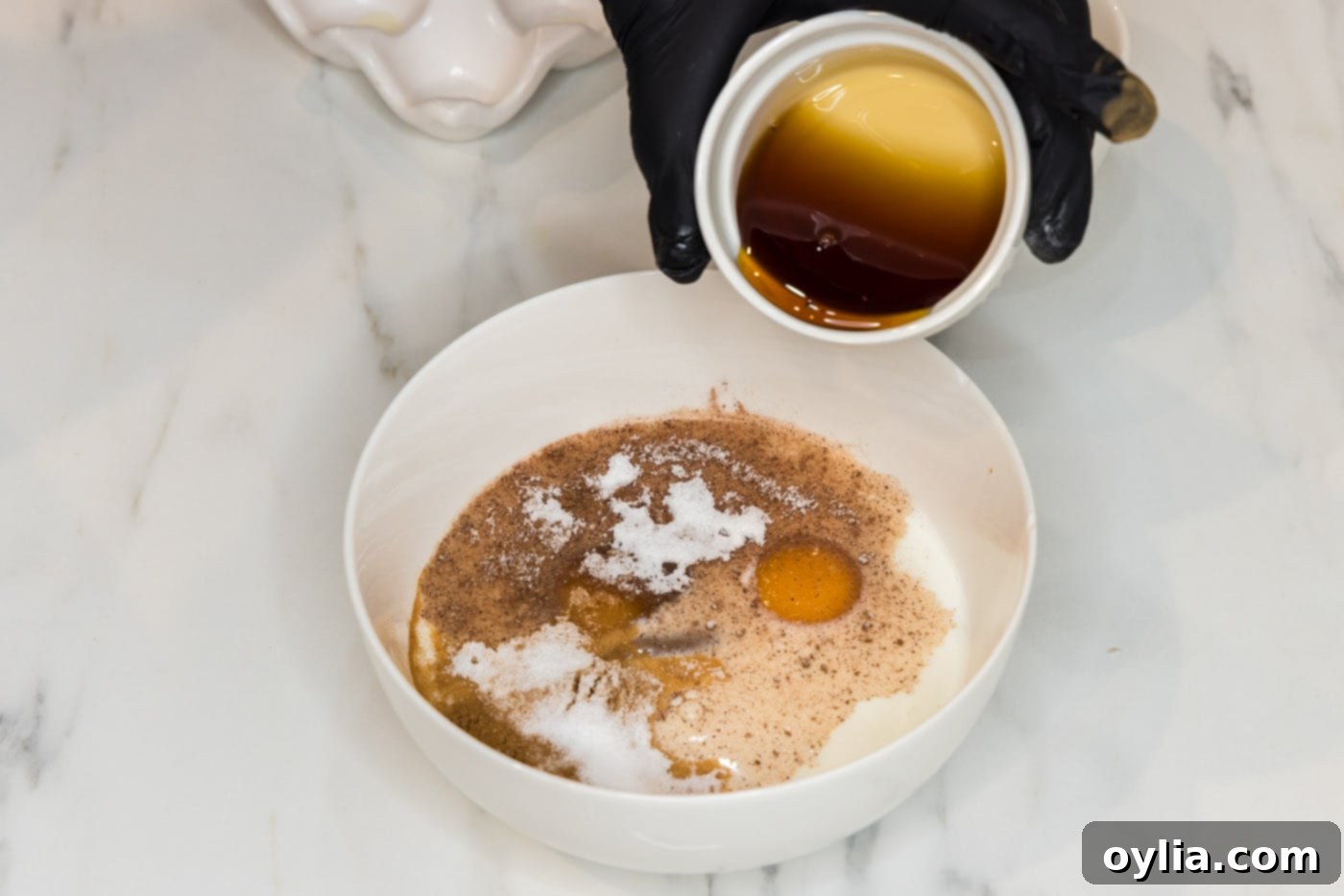 hand pouring maple syrup into French toast batter in a bowl