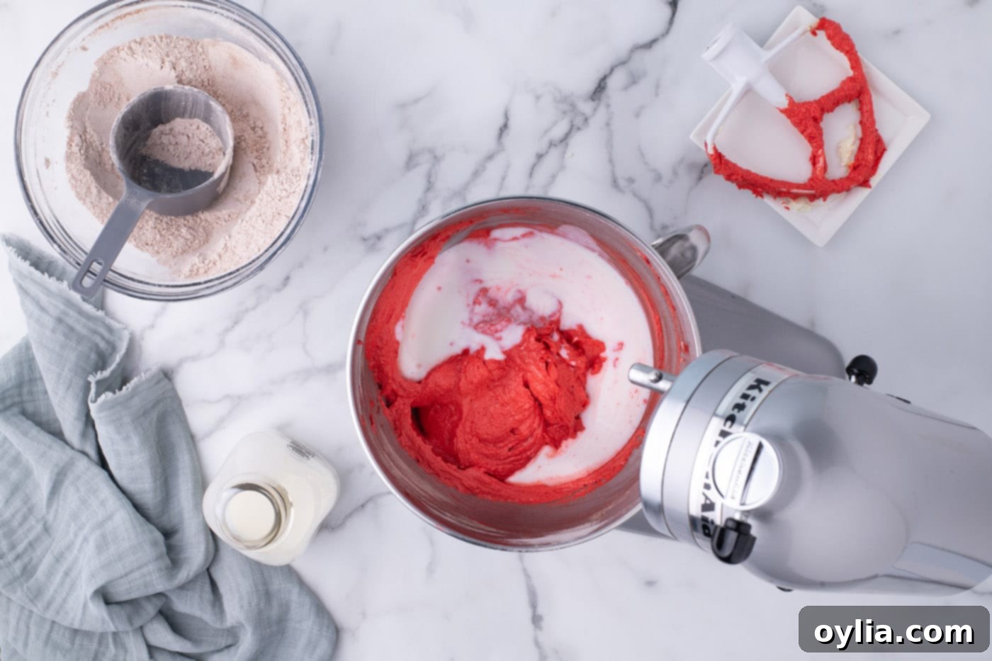 Adding buttermilk to the red velvet cupcake batter during the mixing process