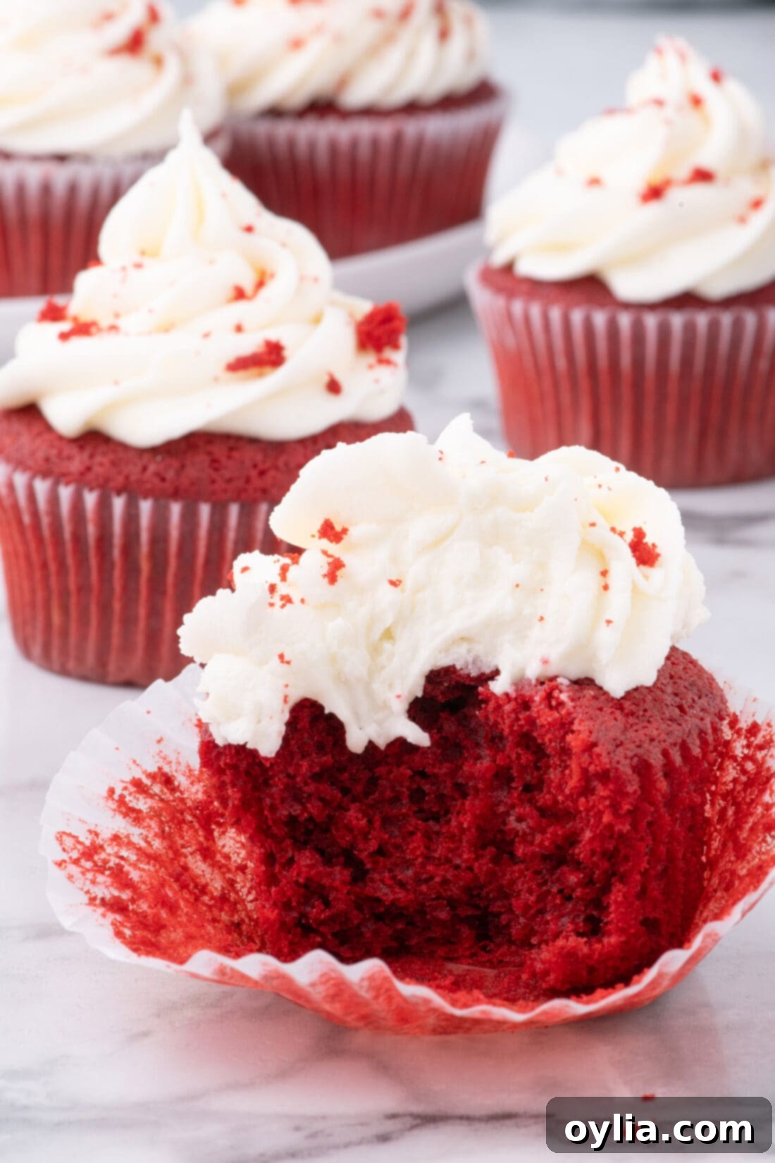 A delicious Red Velvet Cupcake with a bite taken, showing its moist interior and creamy frosting