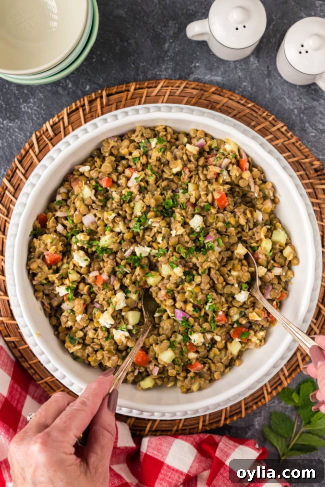 Vibrant Mediterranean Lentil Salad 3 Two hands holding spoons, about to scoop Lentil Salad from a large bowl, showing the vibrant ingredients.