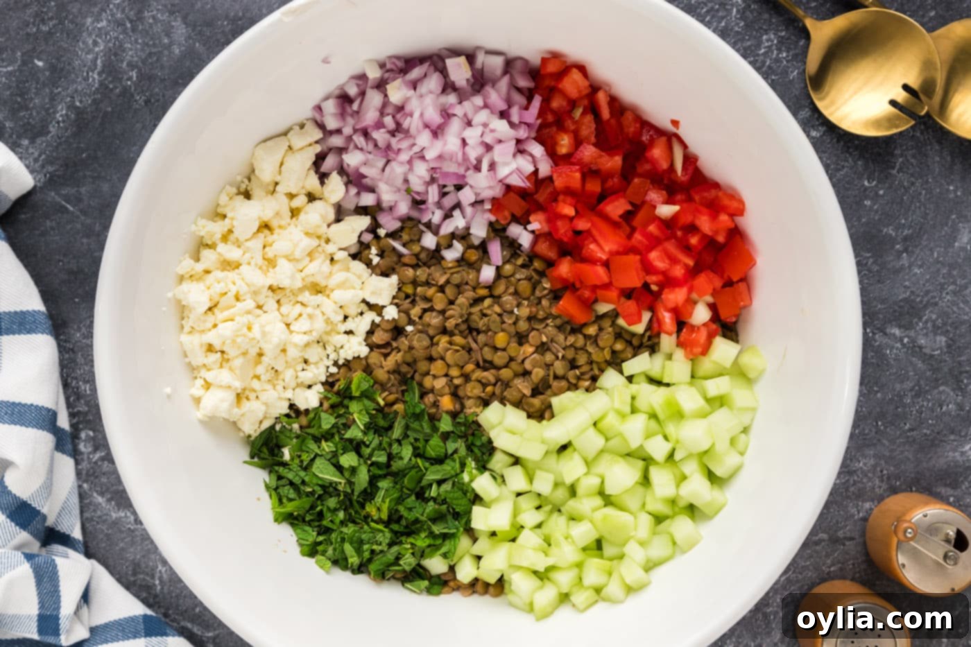 Cooked lentils, diced roma tomatoes, shallots, cucumber, crumbled feta, and fresh mint in a large mixing bowl, ready for dressing.
