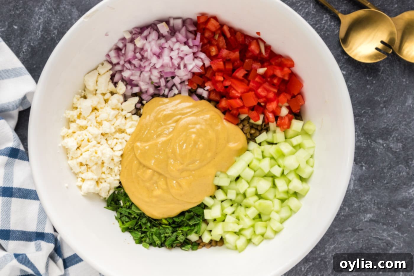 Pouring the homemade dressing over the mixed lentil salad ingredients in a large mixing bowl.