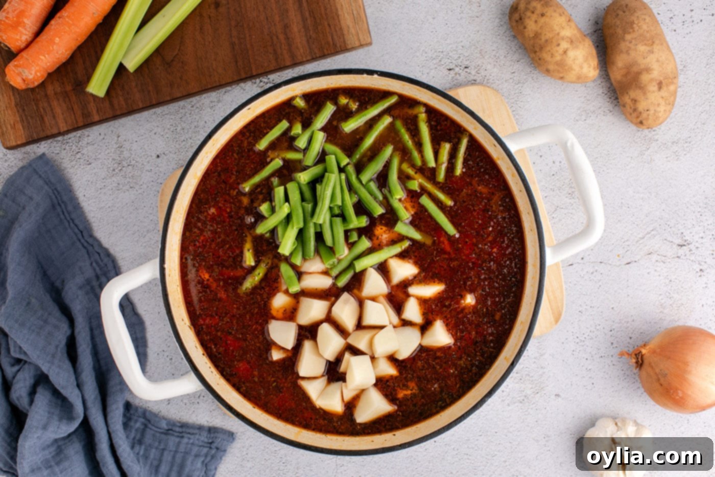 cubed potatoes and trimmed green beans added to vegetable beef soup in pot