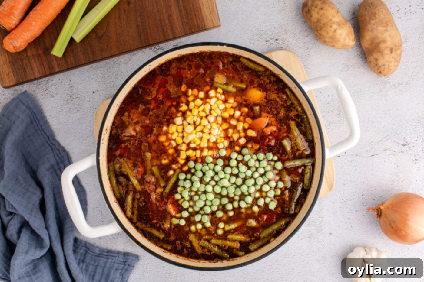 corn and frozen peas added to vegetable beef soup in pot