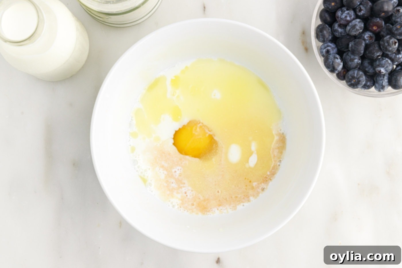 Whisking wet ingredients (egg, melted butter, vanilla, and buttermilk) in a separate bowl to prepare pancake batter.