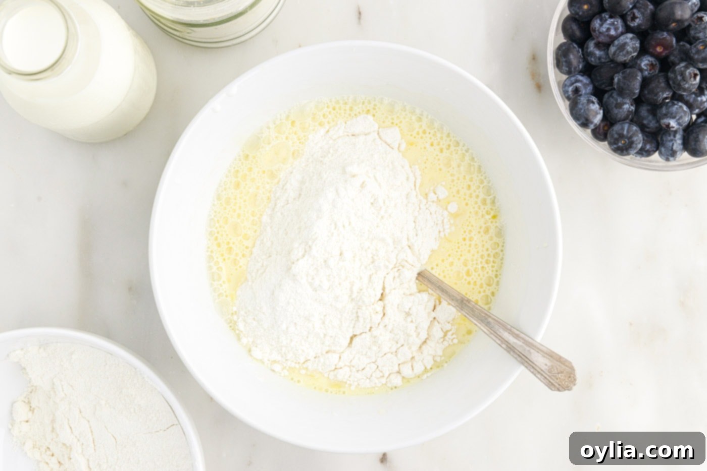 Gently whisking wet and dry ingredients together in a bowl until just combined, showing a slightly lumpy batter, which is ideal for fluffy pancakes.