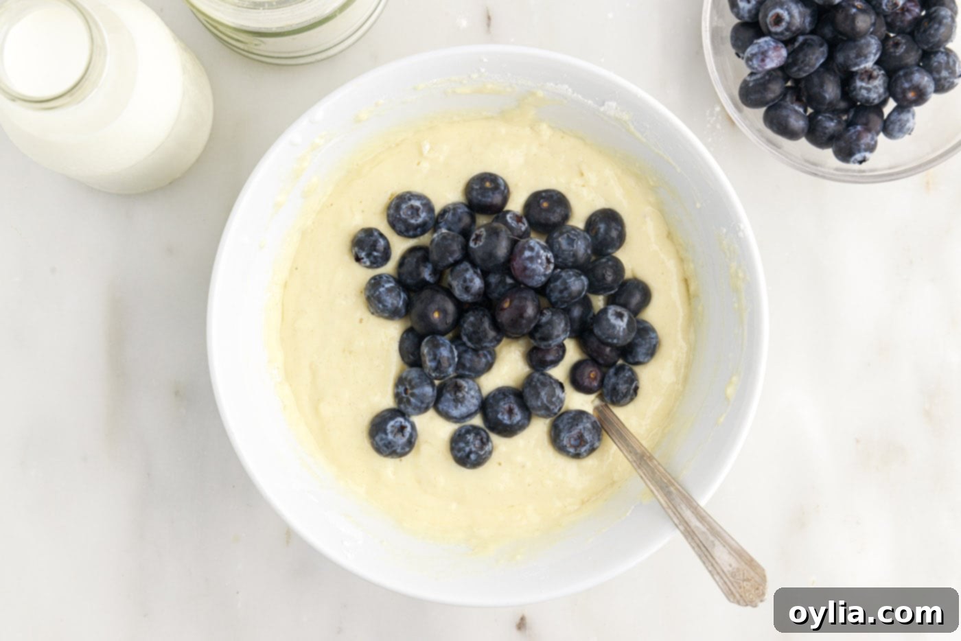 Folding fresh blueberries into the prepared pancake batter with a spatula.