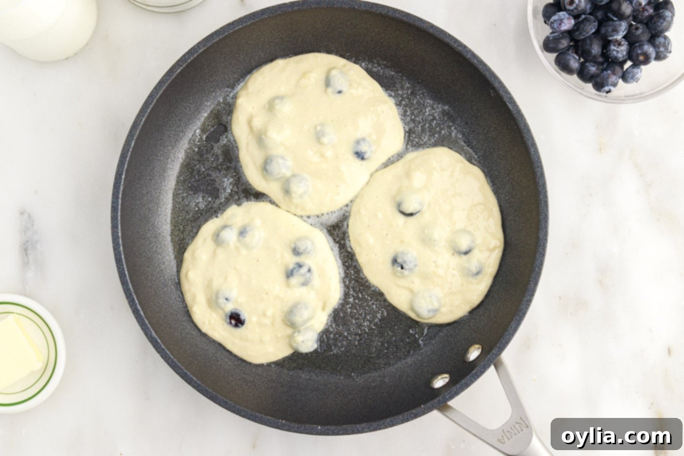 Fresh blueberry pancakes cooking in a skillet, showing the batter starting to bubble.