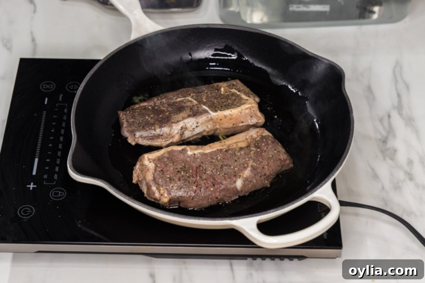 Two sous vide cooked steaks being seared in a hot skillet with olive oil, developing a beautiful crust.