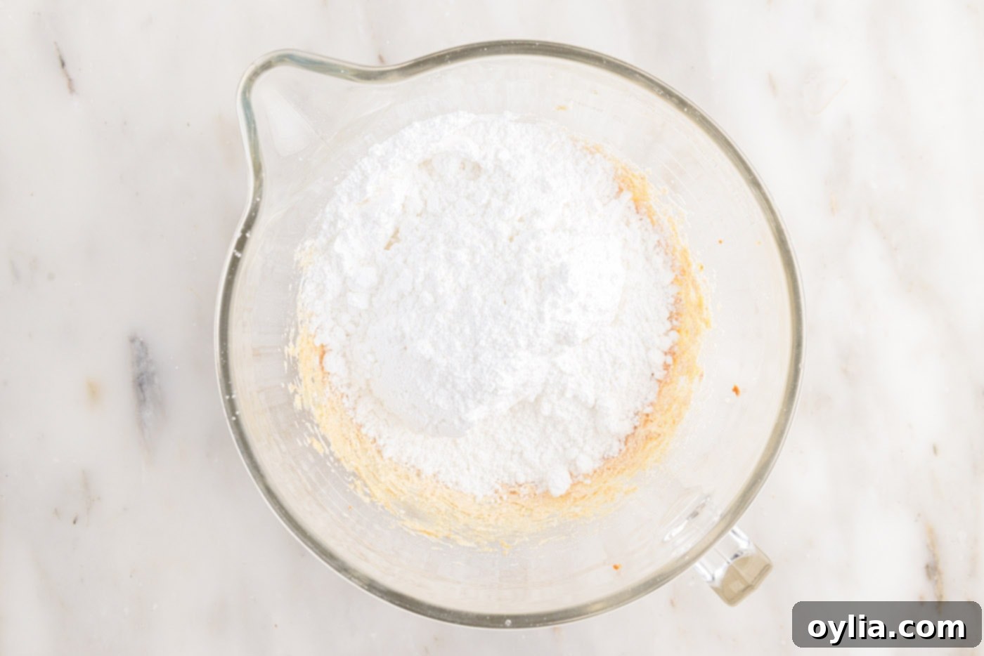 Adding sifted powdered sugar to the whipped brown butter in a stand mixer.