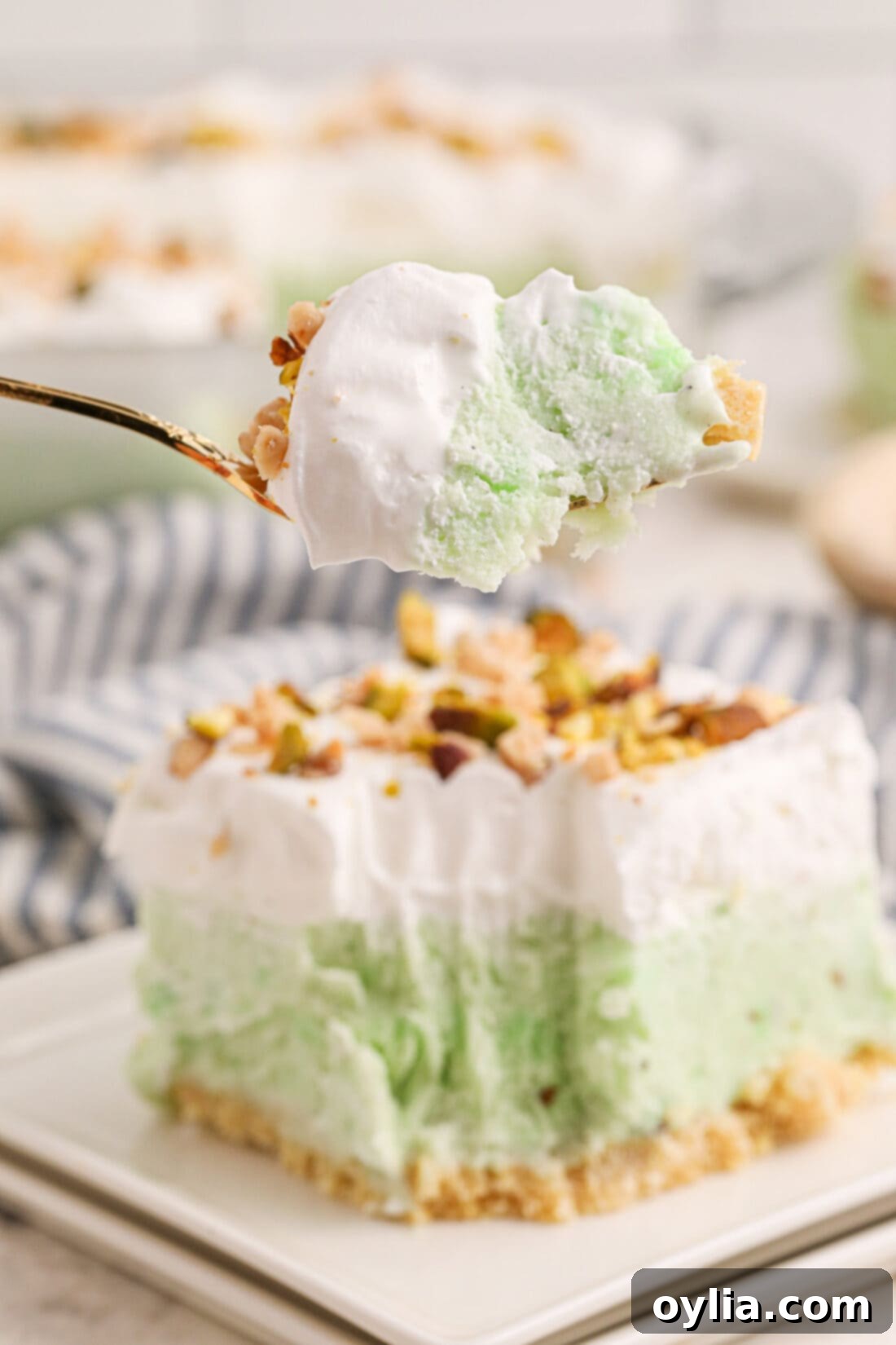 Ultimate Pistachio Ice Cream Cake 2 A delectable slice of Pistachio Ice Cream Cake on a fork, with the full cake in the background on a plate, ready to be served at a summer party.