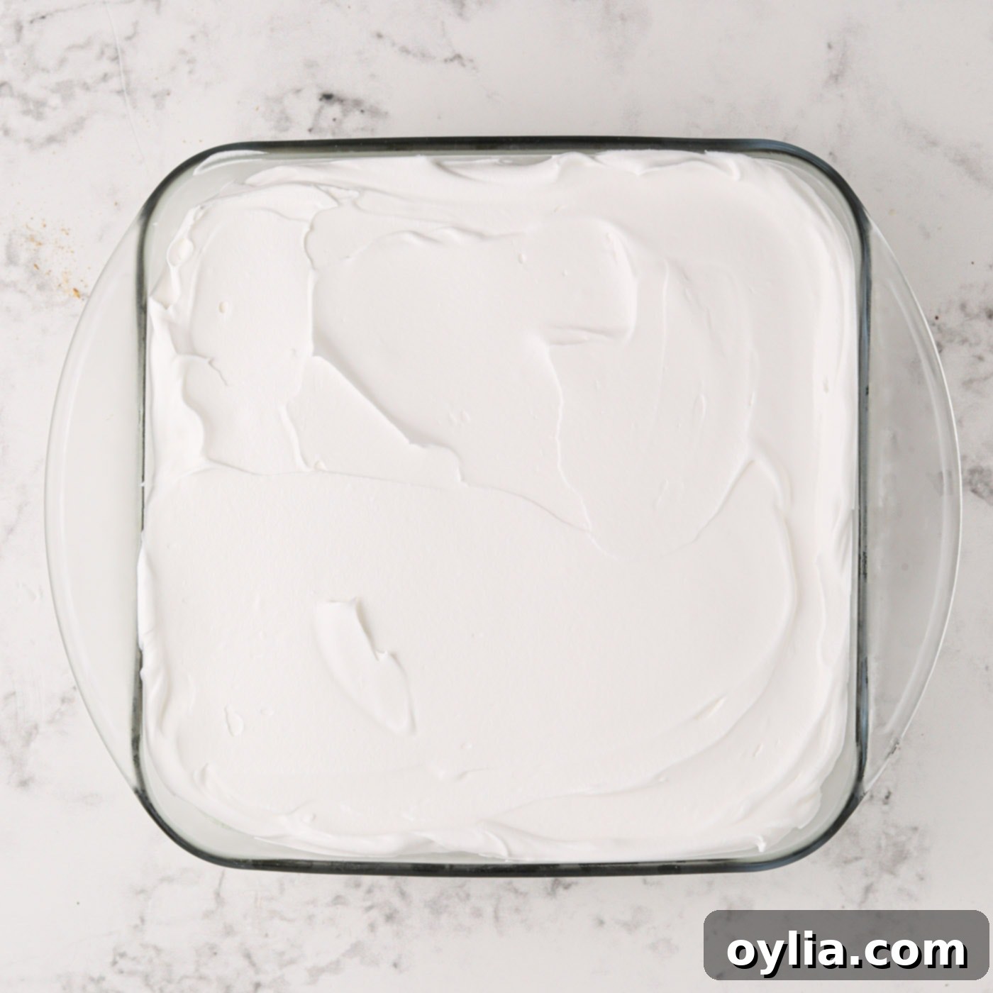 Whipped topping smoothly spread over the pistachio ice cream layer in the baking dish.