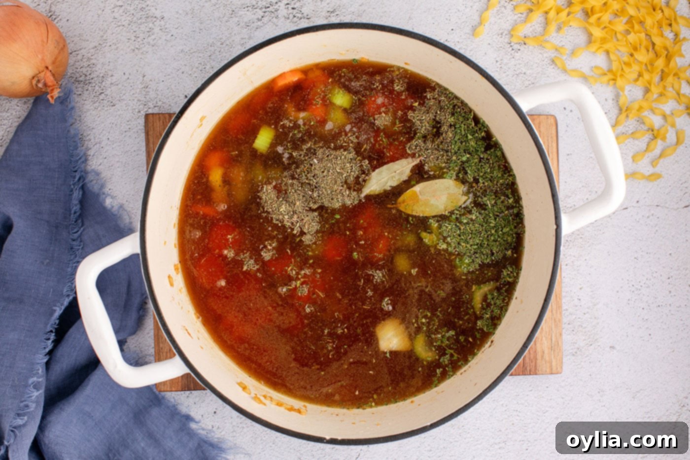Beef broth and various seasonings added to the sautéed vegetable mix in a Dutch oven