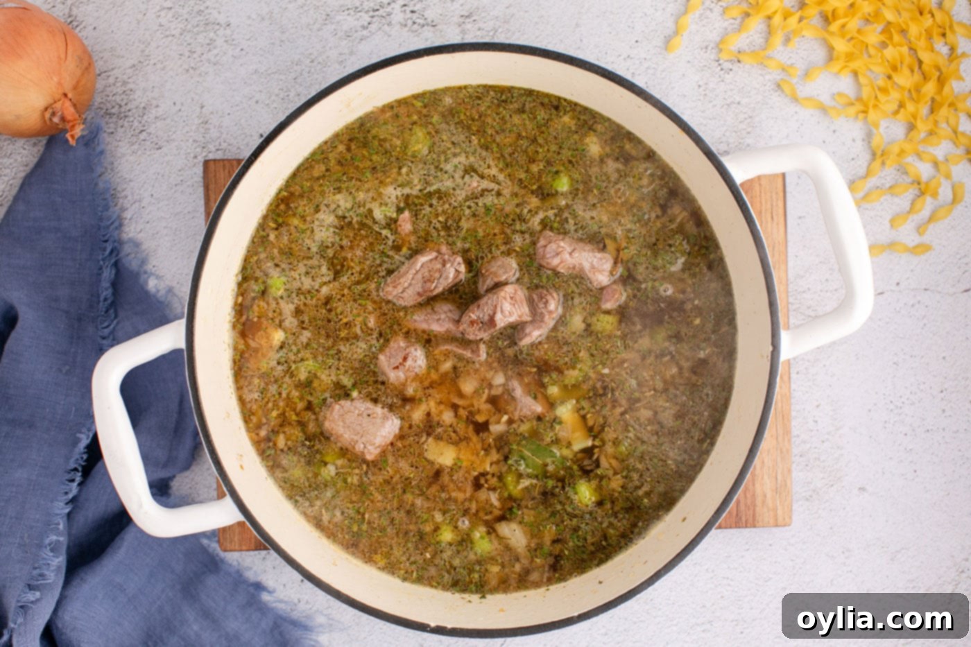 Beef noodle soup simmering gently in a covered pot on the stovetop