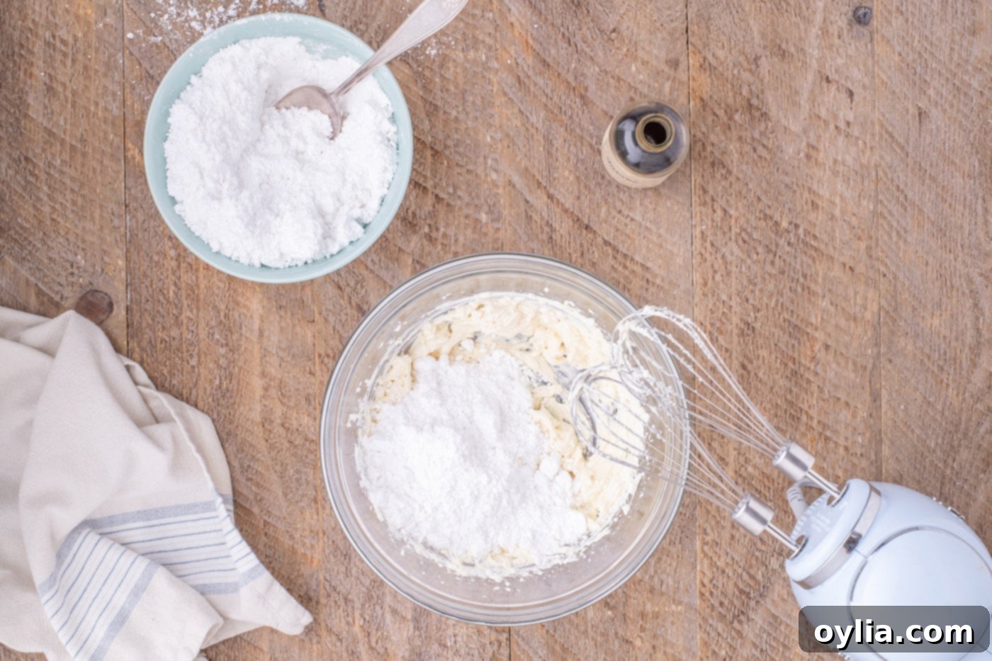 adding powdered sugar to cream cheese frosting in a bowl