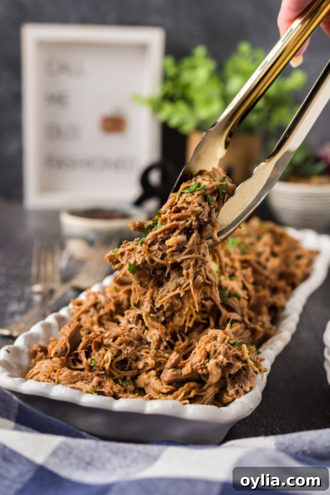 Pulled Pork Perfection 3 Serving tongs lifting a generous portion of freshly shredded pulled pork from a large platter, highlighting its tender, moist texture.