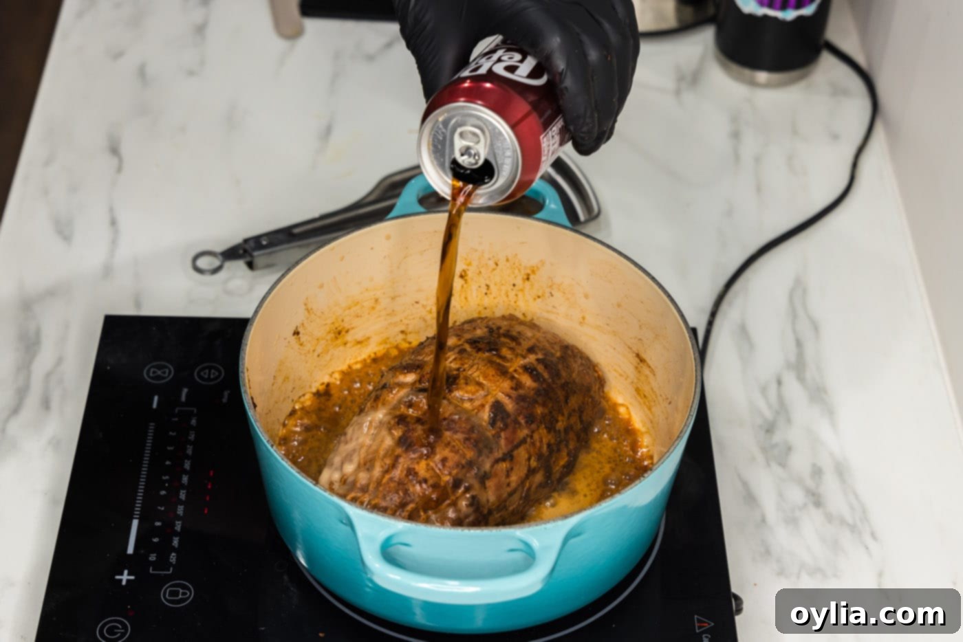 A can of Dr. Pepper being poured directly over the seared pork shoulder in the Dutch oven.