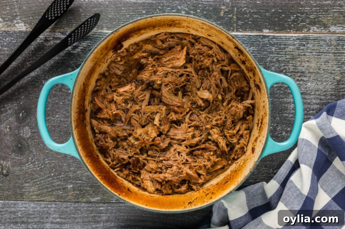 Shredded pulled pork, sitting in its rich cooking juices inside a Dutch oven, ready for the final uncovered bake.