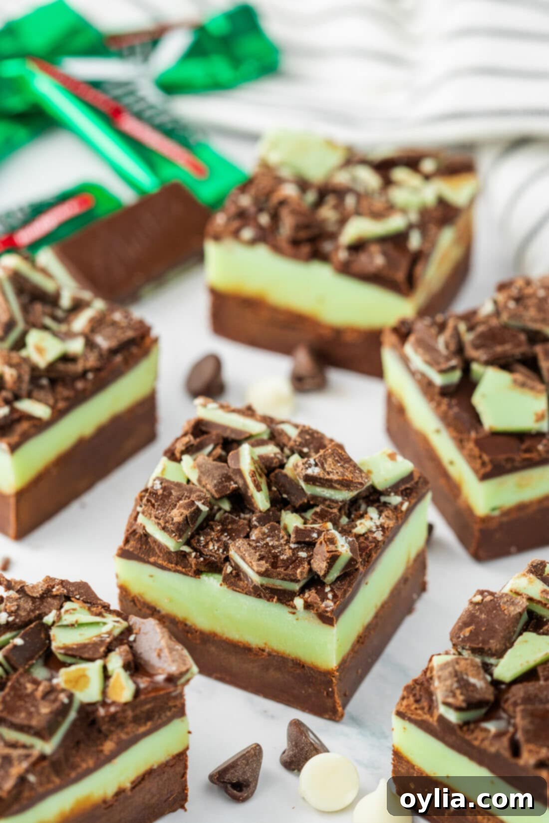 Andes Mint Chocolate Fudge 2 Andes Mint Fudge squares neatly arranged on a table with blurred Andes mint candies in the background, showcasing its vibrant layers
