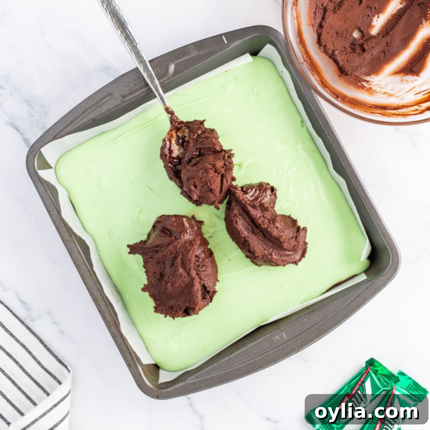 Smoothly spreading the final melted chocolate layer over the green mint fudge in the pan
