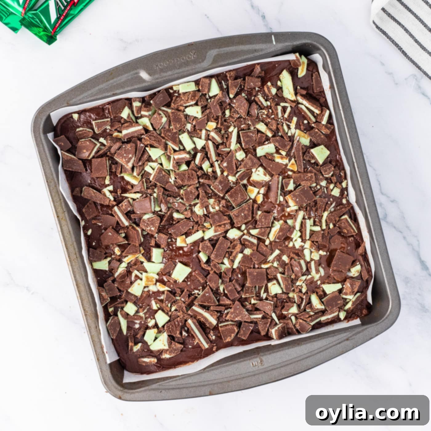 Generously sprinkling chopped Andes mint candies over the freshly spread chocolate fudge topping