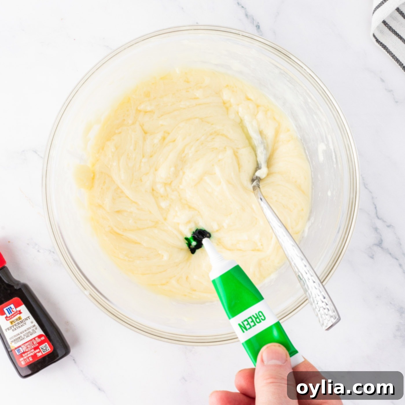 Adding green food coloring and peppermint extract to the melted white chocolate fudge mixture, stirring to combine