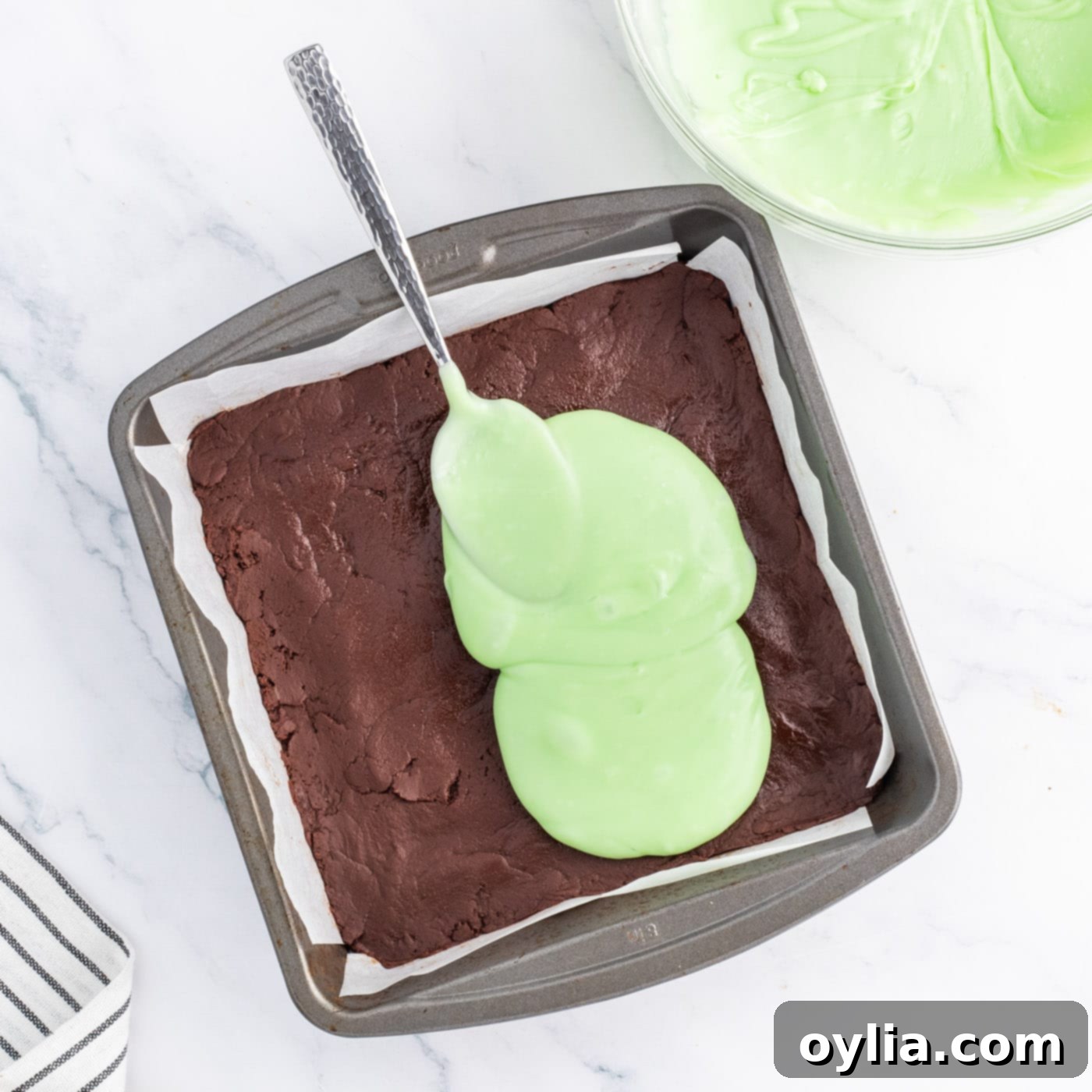 Spreading the bright green mint fudge mixture evenly over the set chocolate layer in the pan