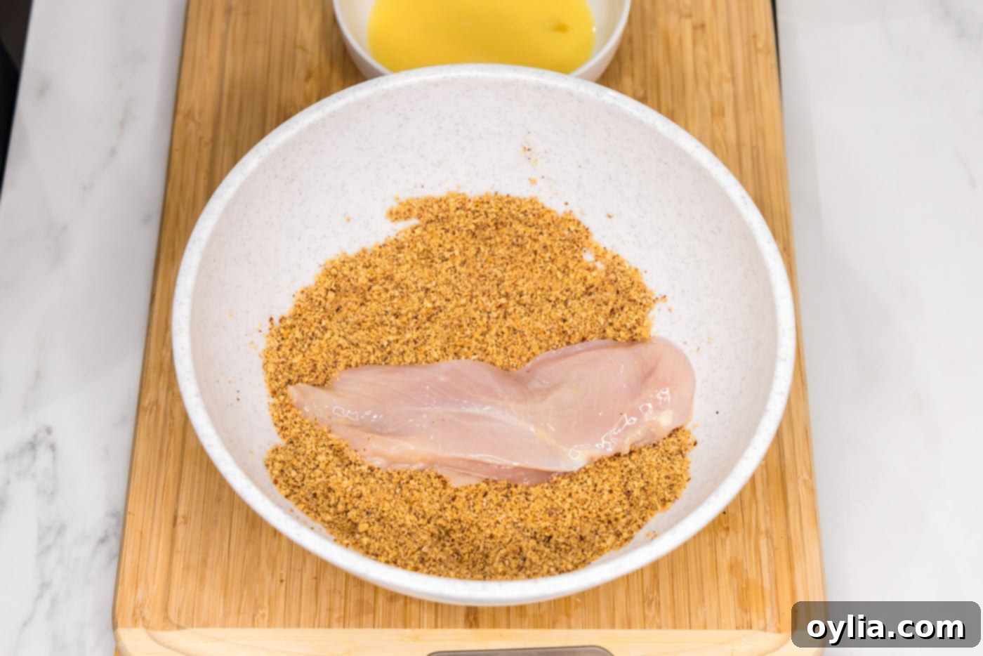 dredging chicken breast in crushed almonds